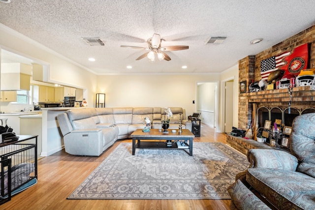 living room with a fireplace, light hardwood / wood-style flooring, a textured ceiling, and ceiling fan