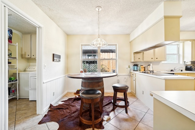 kitchen with cream cabinets, black electric stovetop, a textured ceiling, washer / clothes dryer, and hanging light fixtures