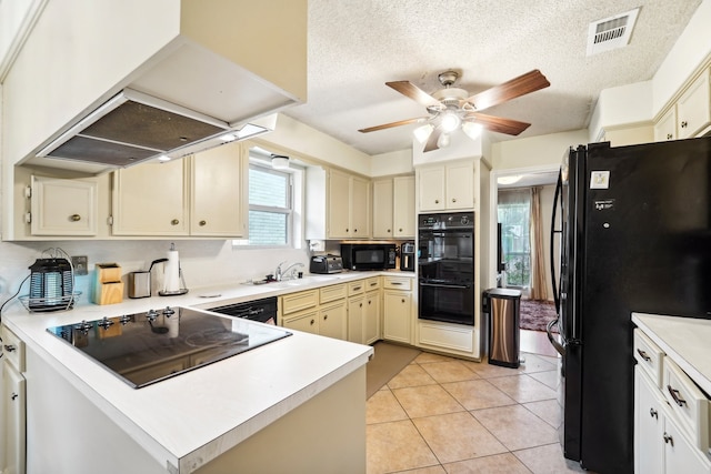 kitchen featuring island range hood, black appliances, cream cabinets, light tile patterned flooring, and a textured ceiling