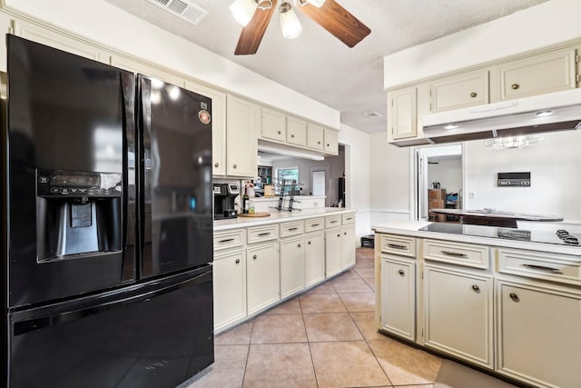 kitchen with black appliances, cream cabinets, light tile patterned flooring, and a textured ceiling