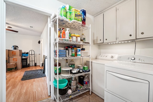 washroom featuring cabinets, light hardwood / wood-style floors, a textured ceiling, and washer and clothes dryer