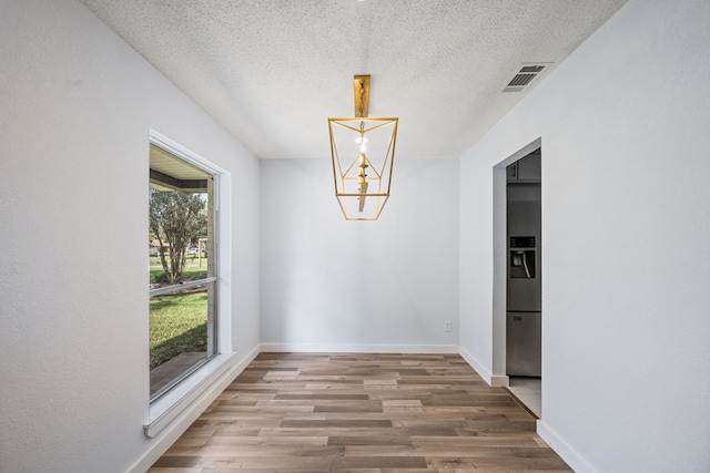 unfurnished dining area with hardwood / wood-style flooring, a textured ceiling, and a notable chandelier