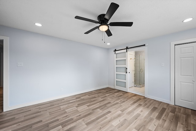 unfurnished bedroom with a textured ceiling, light wood-type flooring, a barn door, and ceiling fan