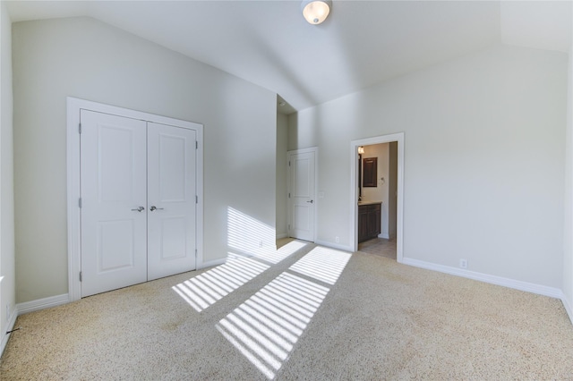 unfurnished bedroom featuring ensuite bath, light carpet, a closet, and lofted ceiling