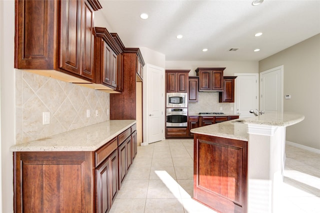 kitchen featuring sink, stainless steel appliances, tasteful backsplash, light stone counters, and an island with sink