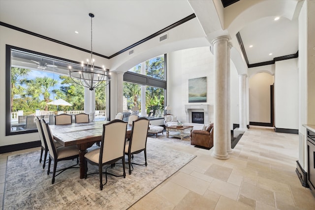 dining space with decorative columns, a chandelier, a large fireplace, and crown molding