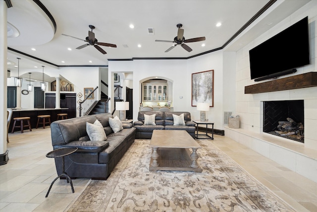 living room featuring ceiling fan, a tiled fireplace, and ornamental molding