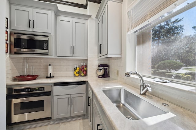 kitchen featuring light stone countertops, sink, decorative backsplash, and appliances with stainless steel finishes