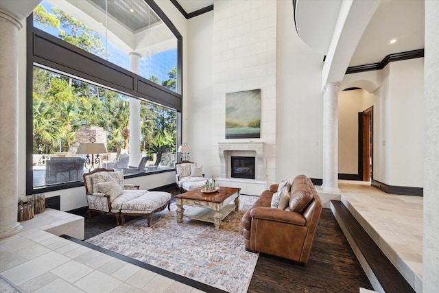 living room with a towering ceiling, plenty of natural light, a tile fireplace, and decorative columns