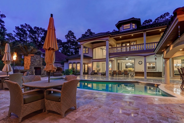 pool at dusk with an outdoor stone fireplace and a patio area