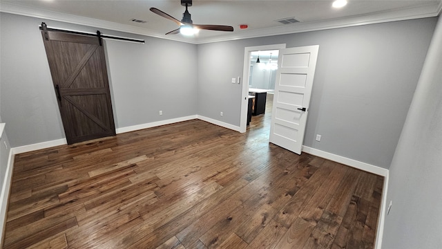 unfurnished bedroom with a barn door, dark hardwood / wood-style flooring, ceiling fan, and crown molding