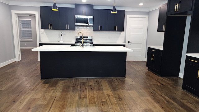 kitchen featuring appliances with stainless steel finishes, tasteful backsplash, hanging light fixtures, a kitchen island with sink, and dark wood-type flooring