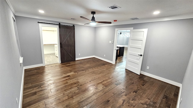 unfurnished bedroom featuring dark wood-type flooring, a barn door, ornamental molding, ceiling fan, and a walk in closet