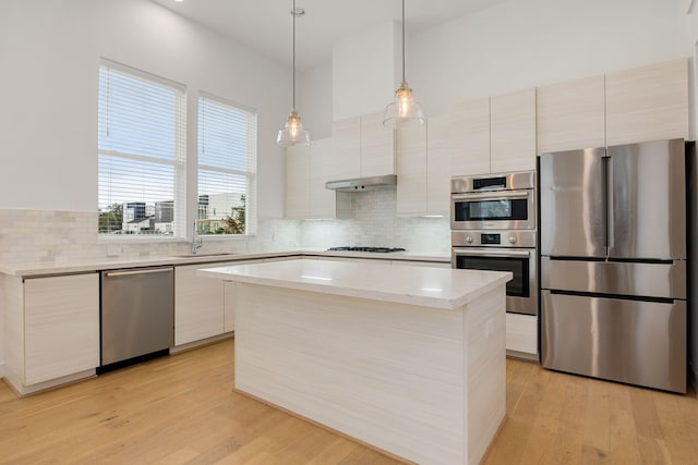 kitchen with light hardwood / wood-style flooring, a kitchen island, appliances with stainless steel finishes, and pendant lighting