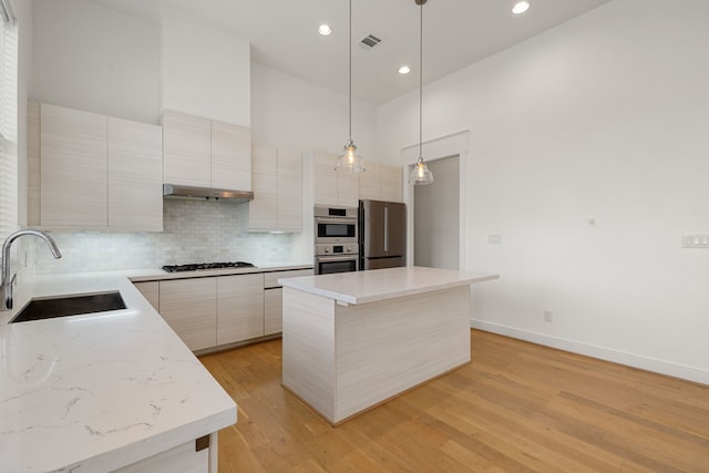 kitchen featuring stainless steel appliances, sink, light hardwood / wood-style flooring, a center island, and hanging light fixtures