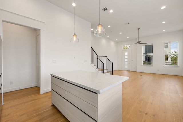 kitchen with light stone counters, ceiling fan, decorative light fixtures, light hardwood / wood-style flooring, and a center island