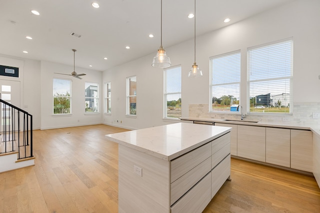 kitchen with tasteful backsplash, sink, light hardwood / wood-style flooring, a center island, and hanging light fixtures