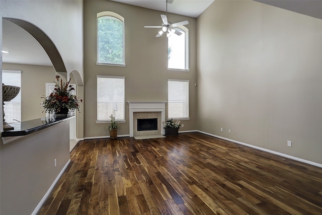 unfurnished living room featuring ceiling fan, a high ceiling, a tiled fireplace, and dark hardwood / wood-style flooring