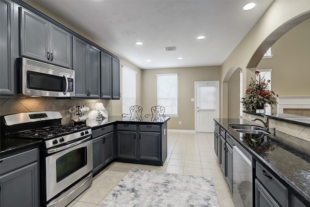 kitchen featuring tasteful backsplash, stainless steel appliances, dark stone counters, light tile patterned floors, and sink