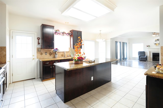 kitchen featuring dark brown cabinetry, decorative light fixtures, a center island, ornate columns, and decorative backsplash