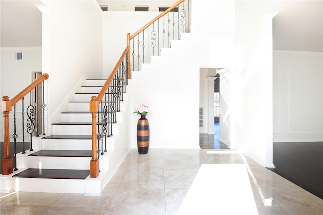 staircase featuring a towering ceiling and crown molding