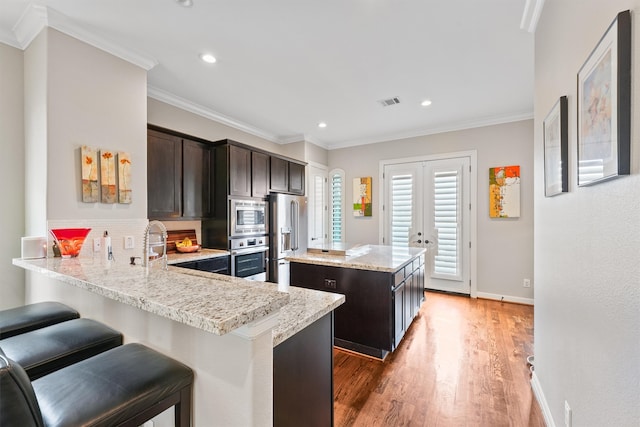 kitchen featuring appliances with stainless steel finishes, dark brown cabinetry, hardwood / wood-style flooring, kitchen peninsula, and a center island