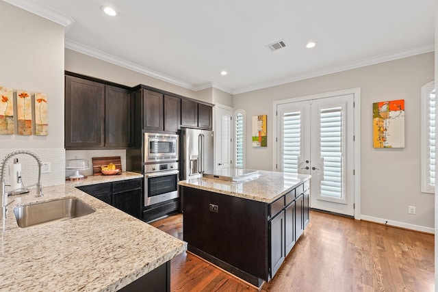 kitchen with light stone counters, stainless steel appliances, sink, hardwood / wood-style flooring, and a center island