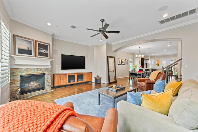 living room with a stone fireplace, wood-type flooring, and crown molding