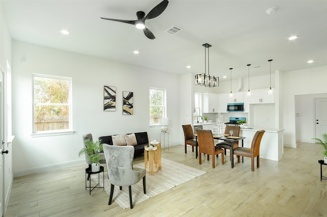 living room with a wealth of natural light, ceiling fan with notable chandelier, and light hardwood / wood-style flooring