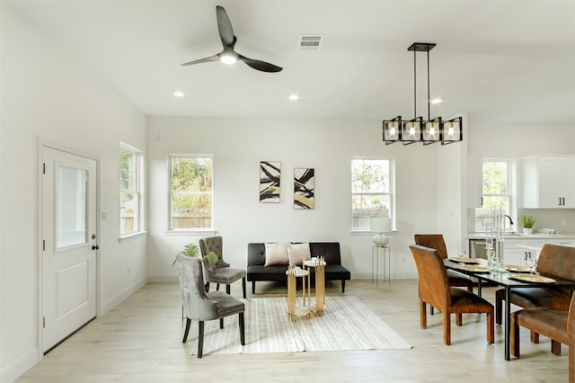 dining area featuring ceiling fan with notable chandelier, light hardwood / wood-style flooring, a healthy amount of sunlight, and sink