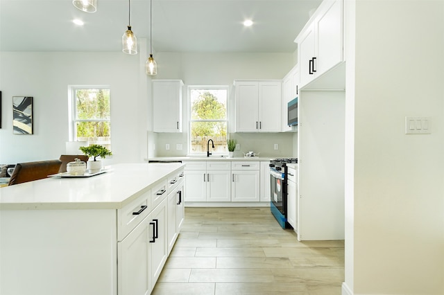 kitchen with black appliances, a center island, white cabinetry, hanging light fixtures, and light hardwood / wood-style flooring