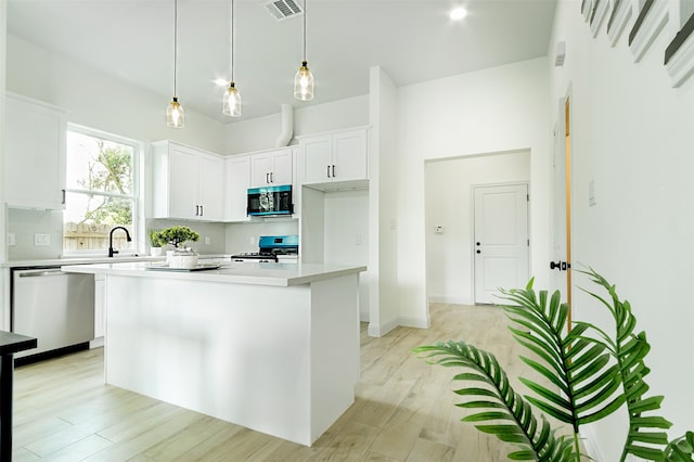 kitchen featuring stainless steel appliances, white cabinets, hanging light fixtures, a kitchen island, and light hardwood / wood-style flooring