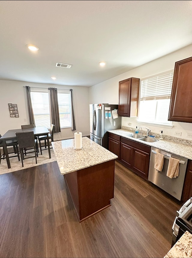 kitchen featuring stainless steel appliances, dark wood-type flooring, light stone counters, a center island, and sink