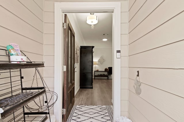 hall featuring hardwood / wood-style flooring, wooden walls, and ornamental molding