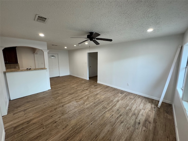 unfurnished living room featuring dark wood-type flooring, a textured ceiling, and ceiling fan