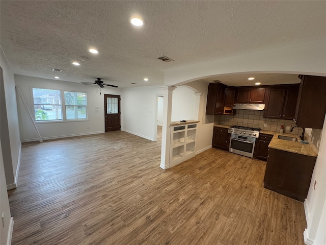 kitchen with stainless steel gas range, a textured ceiling, light wood-type flooring, and decorative columns