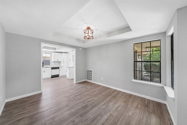 unfurnished living room featuring a wealth of natural light, wood-type flooring, and a tray ceiling