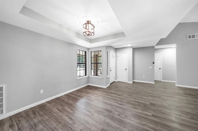 empty room featuring dark hardwood / wood-style floors, a chandelier, and a tray ceiling