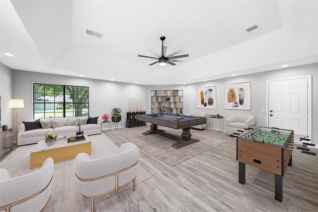 recreation room with pool table, light wood-type flooring, ceiling fan, and a tray ceiling