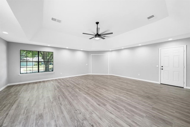 spare room with a raised ceiling, ceiling fan, and light hardwood / wood-style flooring