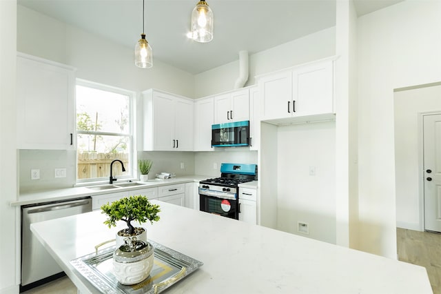 kitchen with stainless steel appliances, white cabinets, hanging light fixtures, sink, and light wood-type flooring