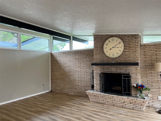 unfurnished living room with a brick fireplace, hardwood / wood-style flooring, a healthy amount of sunlight, and a textured ceiling