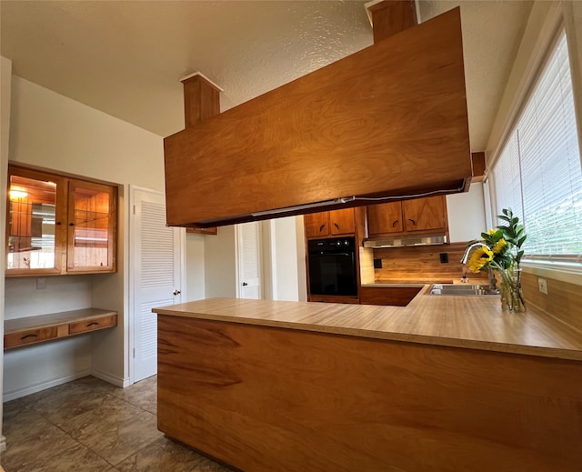 kitchen with black oven, light tile patterned floors, decorative backsplash, sink, and kitchen peninsula