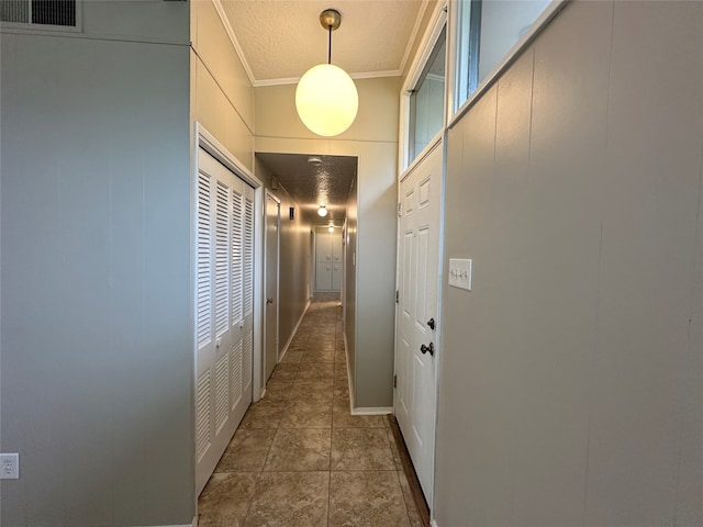 hallway with ornamental molding, dark tile patterned flooring, and a textured ceiling