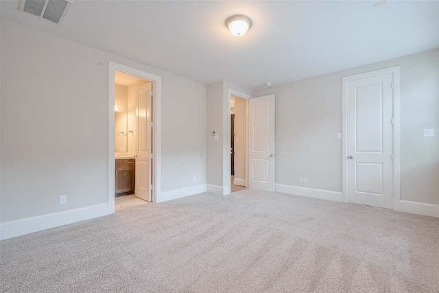 unfurnished bedroom featuring connected bathroom, a closet, and light colored carpet