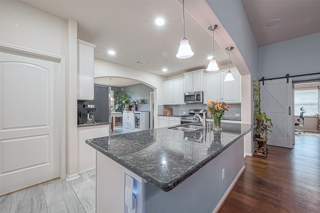 kitchen featuring white cabinetry, a barn door, a center island with sink, and stainless steel appliances