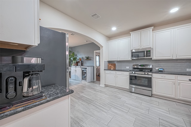 kitchen with dark stone counters, white cabinetry, backsplash, and stainless steel appliances