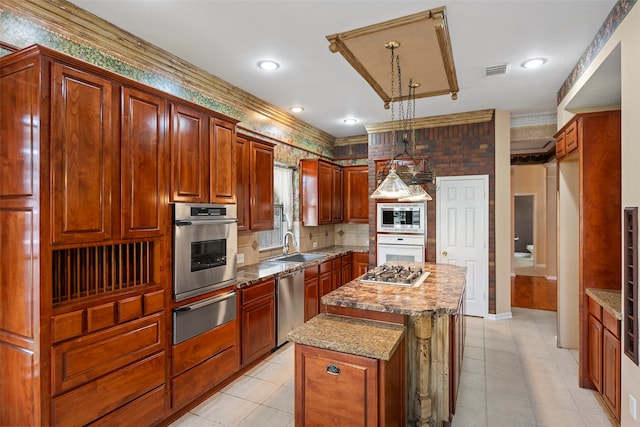 kitchen with sink, hanging light fixtures, light stone countertops, appliances with stainless steel finishes, and a kitchen island