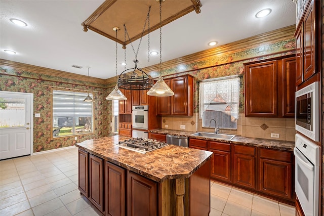 kitchen with light stone counters, stainless steel appliances, sink, decorative light fixtures, and a center island