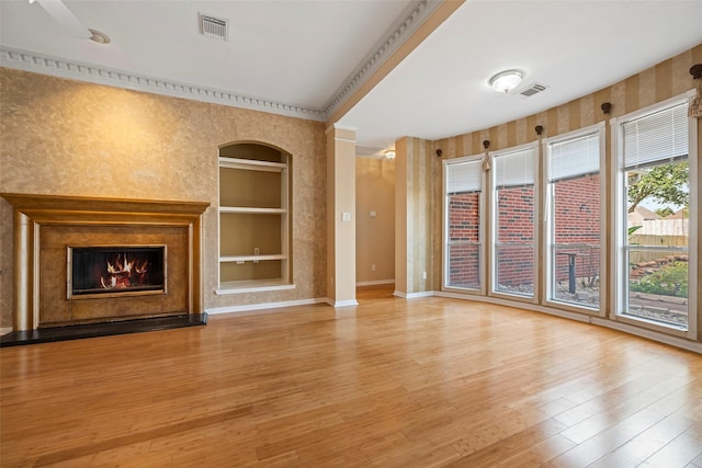 unfurnished living room featuring built in shelves, light wood-type flooring, and ornamental molding